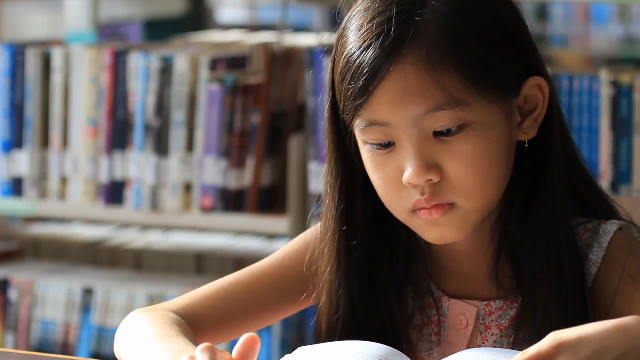 little-asian-girl-reading-a-book-in-library-SBV-301718555-HD